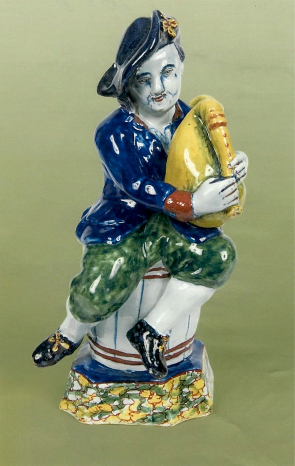 A Dutch Delft polychrome figure of a bagpipe-player seated on a barrel